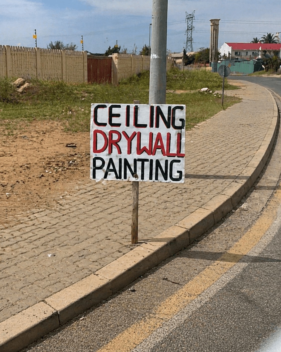 Handmade roadside sign advertising ceiling, drywall and painting services near a building material shop